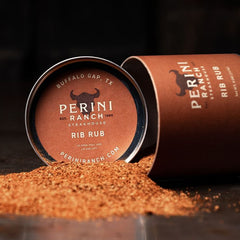 A shaker of Perini Ranch Rib Rub spice mix spilled open with visible spices pouring out onto a surface.